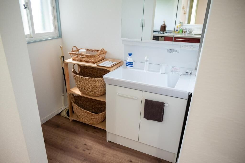 Un bagno piccolo e pulito con un lavandino bianco, uno specchio e cesti di vimini su scaffali.