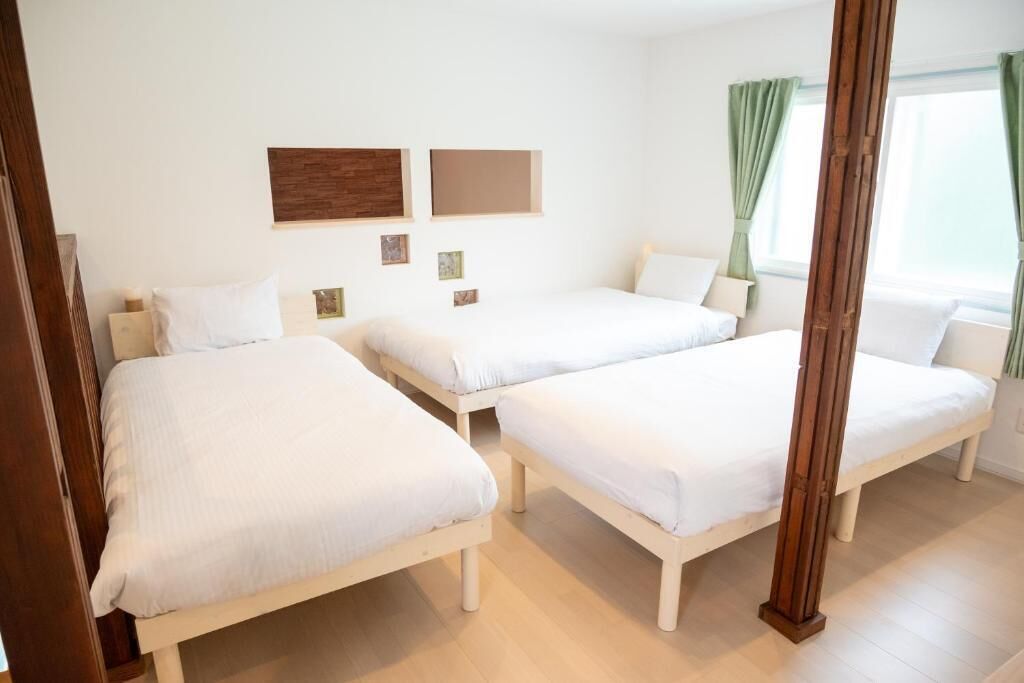 Habitación de hotel con dos camas individuales, suelo de madera, ventana con cortinas y un muro con cuadros.