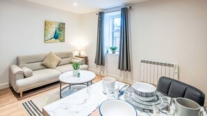 A modern living room with a sofa, a round coffee table, a dining table set with plates, cups, and a chair. - Fishertown Apartment by Interhome (Nairn)