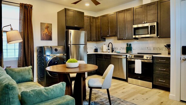 A modern kitchen with dark wooden cabinets, stainless steel appliances, and a dining area with a round table and chairs.