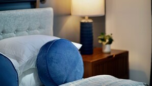 A bedroom with a tufted headboard, a bedside lamp, and a small plant on a wooden nightstand.