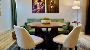 A room with a round wooden table, two white chairs, a green sofa, and two wall-mounted paintings of animals.