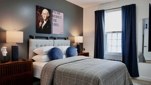 A bedroom with a large bed, two bedside tables, a nightstand, a wall-mounted artwork, a window with curtains, and a wall-mounted radiator.