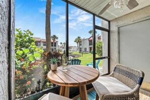 A patio area with a round wooden table and wicker chairs, overlooking a residential neighborhood with houses and palm trees. - Closest to Beach • New Remodel • Pickleball Tennis (Bradenton Beach)