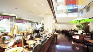 Un espace buffet comprenant plusieurs points de service, un bar à boissons et un coin salon avec des tables et des chaises.