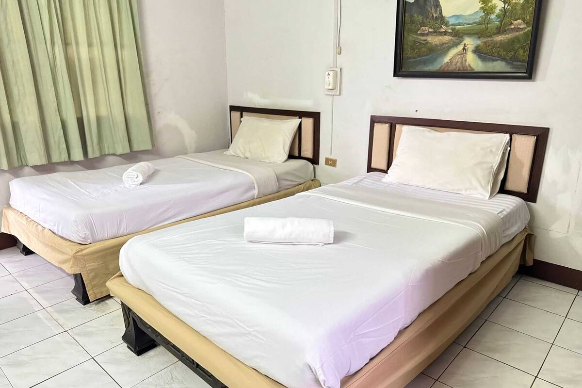 Two single beds with white linens and pillows, a painting on the wall, and a green curtain.