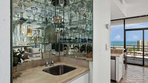 A kitchen with a glass display of various glassware, a sink, and a view of the ocean through a large window.