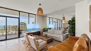 A modern living room with a large TV, comfortable seating, and a view of the ocean.