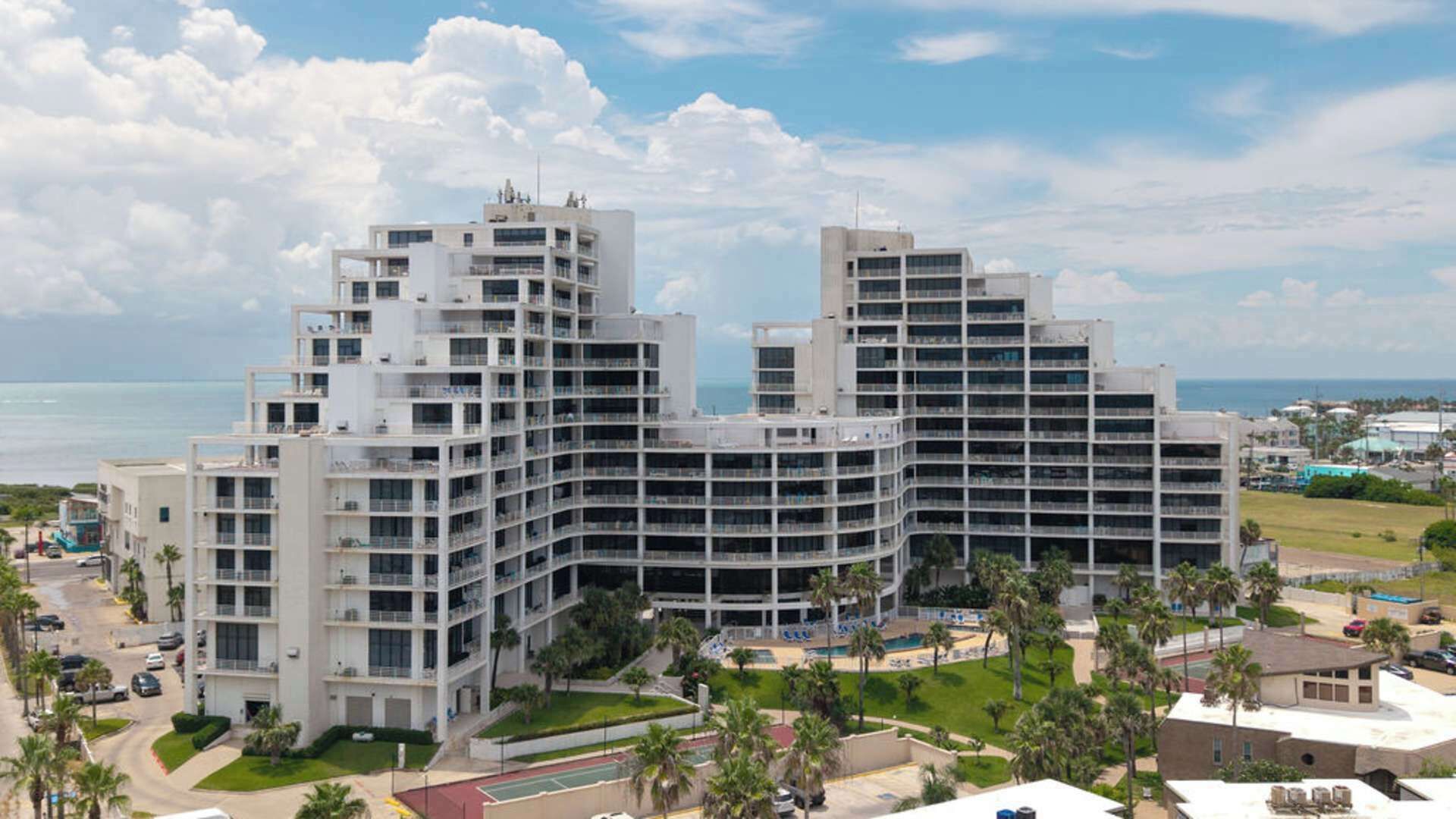 A modern hotel with multiple floors, a pool area, and a view of the ocean.
