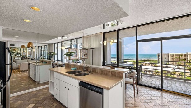 A modern kitchen with a large island, a dishwasher, and a view of the ocean.