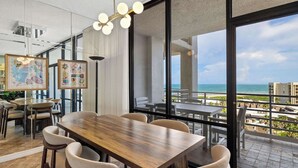 A modern dining area with a wooden table and chairs, large windows with a view of the ocean, and artwork on the walls.
