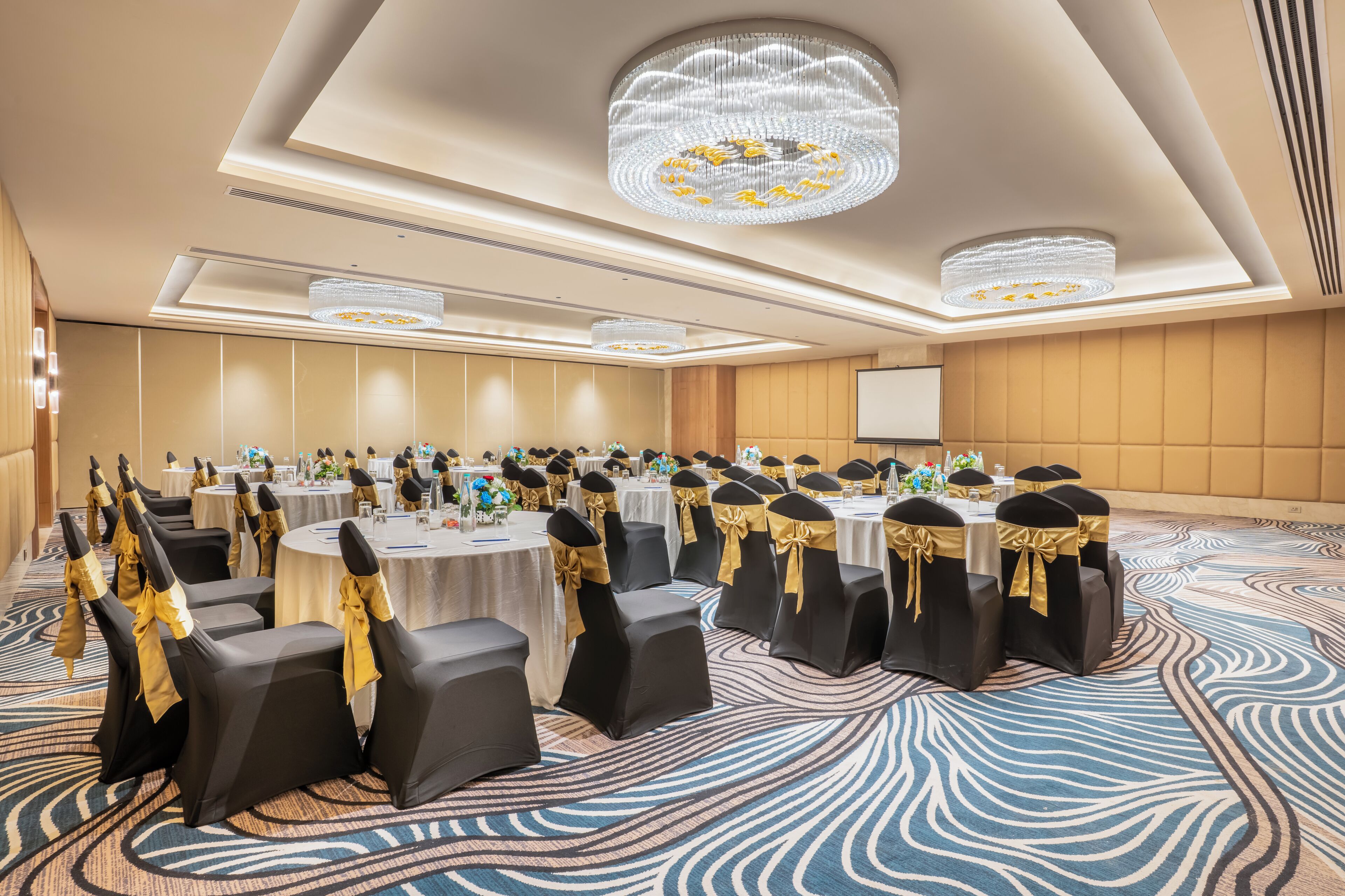 A conference room with round tables, black chairs with gold sashes, and chandeliers.