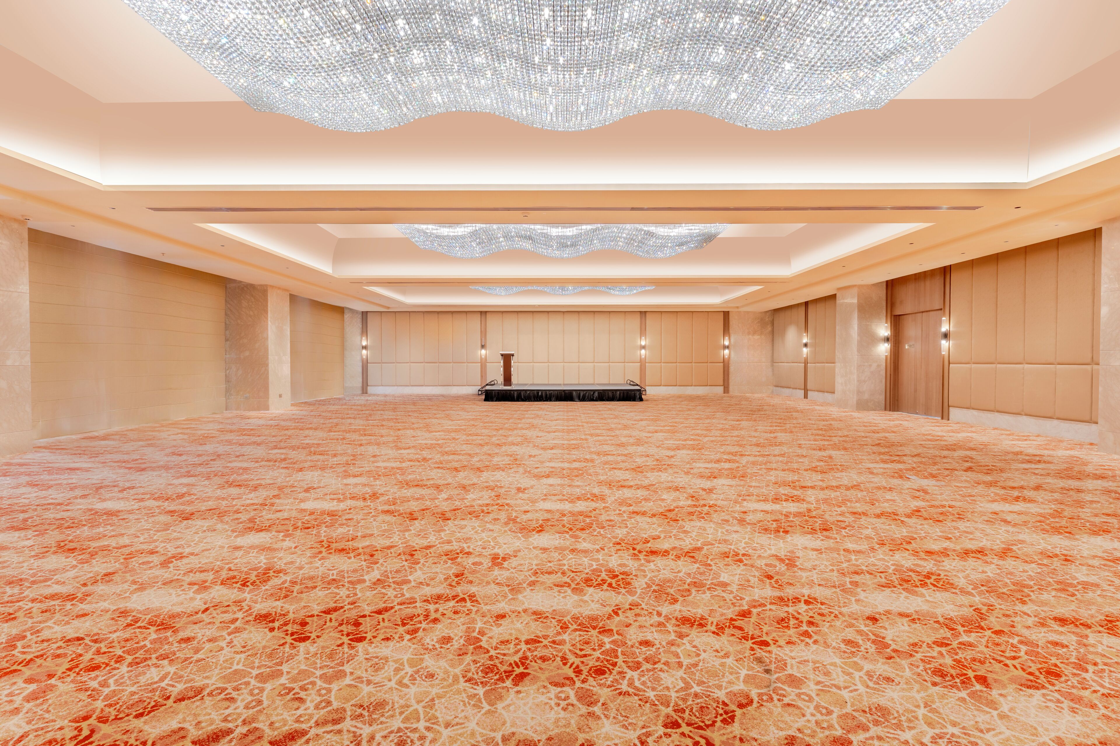 A spacious, well-lit room with a patterned carpet, a large chandelier, and a long row of wooden paneling on the walls.