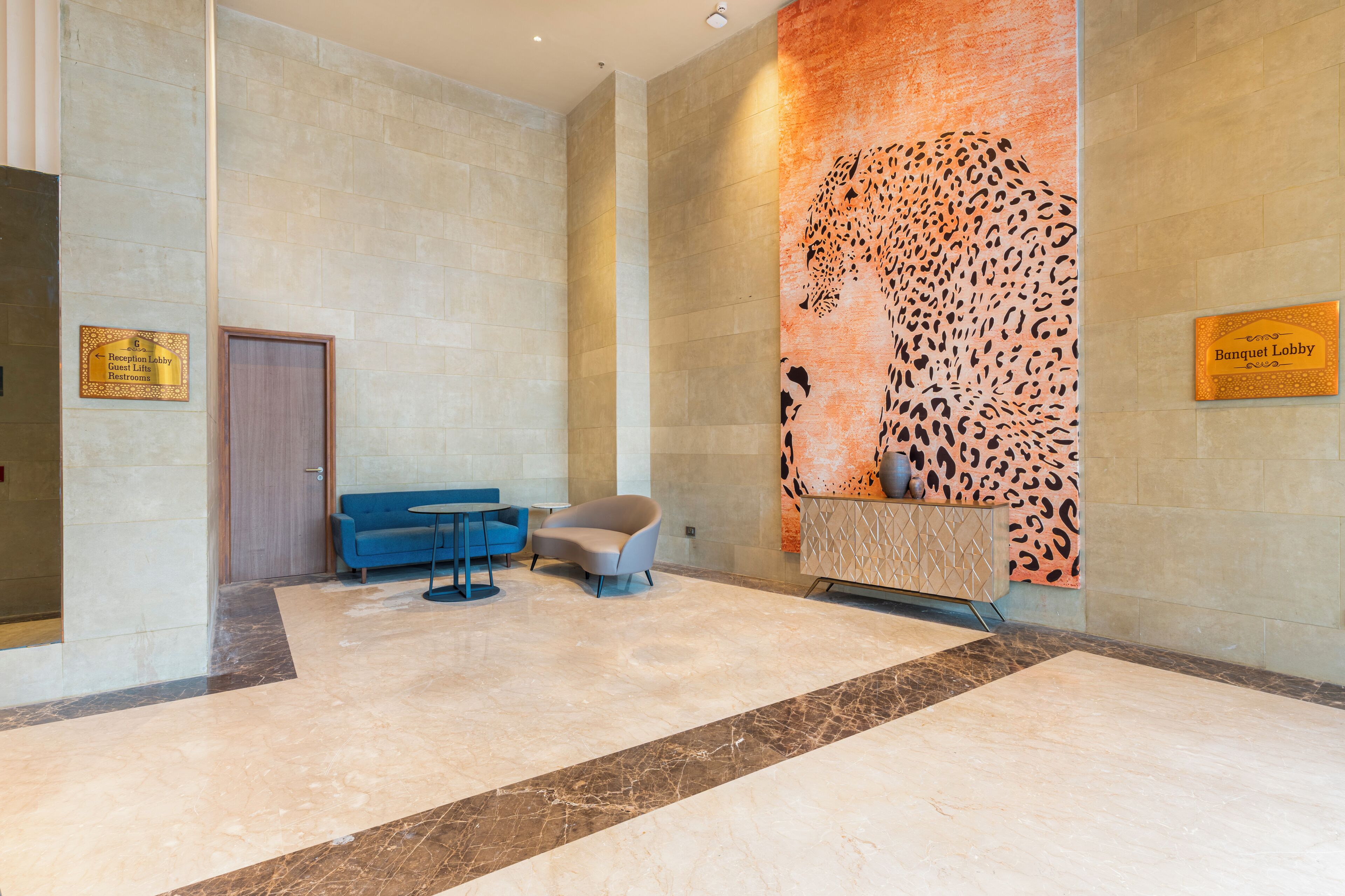 A lobby with a reception desk, a blue sofa, a patterned wall, and a marble floor.