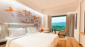 A hotel room with a large bed, a sofa, a small table, and a view of a cityscape through a large window. - Sarovar Premiere Alwar (Alwar)