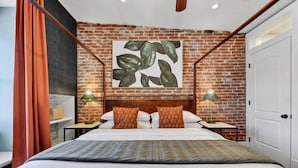 Habitación de hotel con pared de ladrillo, una cama grande con ropa de cama estampada, dos mesitas de noche con lámparas y una puerta blanca.
