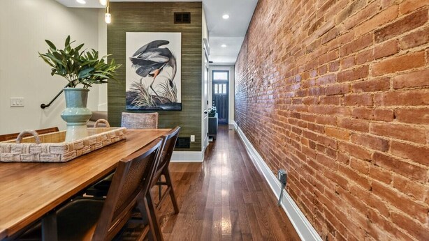 Un comedor con una mesa de madera, sillas, una planta en maceta y una lámpara de pared.