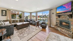 A spacious living room with a fireplace, large windows, and a flat-screen TV.