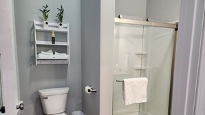 Et moderne badeværelse med toilet, bruseniche i glas og et hvidt håndklæde hængende på døren.