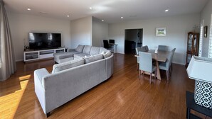 Ein modernes Wohnzimmer mit einer Eckcouch, einem Flachbildfernseher und einem Essbereich mit Tisch und Stühlen.