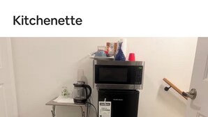 A kitchenette with a microwave, refrigerator, coffee maker, and a small table with a trash bin.