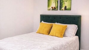 A neatly made bed with a white duvet and two yellow pillows, a green upholstered headboard, and a patterned rug on a wooden floor.