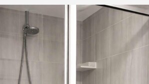 A modern shower with a glass door, grey tiles, and a handheld showerhead.