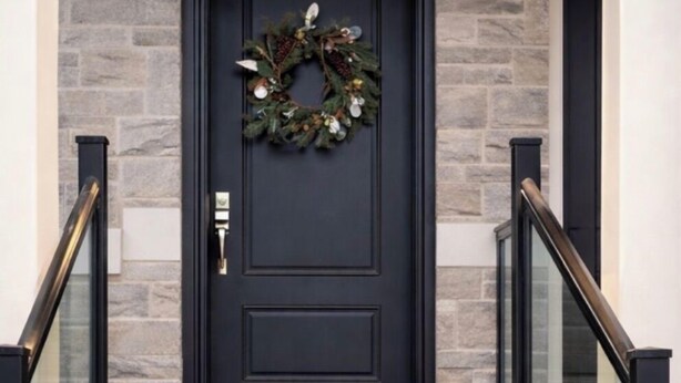 A black door with a wreath, flanked by stone walls and glass railings on a staircase.