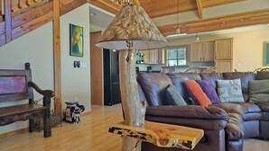 A spacious living room with a wooden ceiling, a brown leather sofa, and a unique lamp made from a tree trunk. - Spacious Family Mountain Cabin ~Fireplace ~2 Decks ~Near Lake (Munds Park)