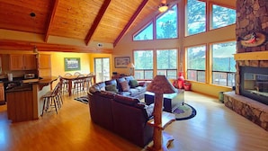A spacious living area with a fireplace, large windows, a dining area, and a kitchen. - Spacious Family Mountain Cabin ~Fireplace ~2 Decks ~Near Lake (Munds Park)