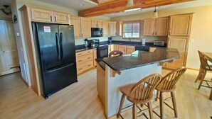 A modern kitchen with wooden cabinets, a black refrigerator, a microwave, and a wooden island with bar stools. - Spacious Family Mountain Cabin ~Fireplace ~2 Decks ~Near Lake (Munds Park)