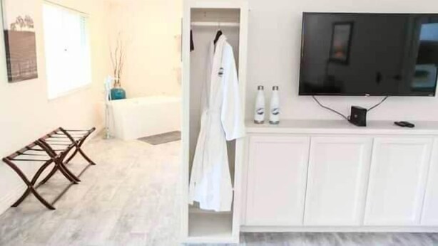 Une salle de bain moderne dotée d’une baignoire, d’un espace douche et d’un meuble-lavabo blanc avec un téléviseur à écran plat.
