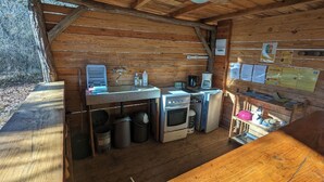 A compact kitchen with a stove, oven, and sink, wooden walls, and a small refrigerator. - Cabanes Sainte Camelle (Saint Victor Rouzaud)