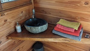 A wooden cabin interior with a stone sink, a window, a mirror, and a small trash bin. - Cabanes Sainte Camelle (Saint Victor Rouzaud)
