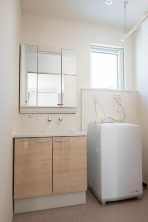A bathroom with a mirror, a sink, a cabinet, and a white appliance, possibly a water heater or heater. - Lighthouse Asahikawa (Asahikawa)