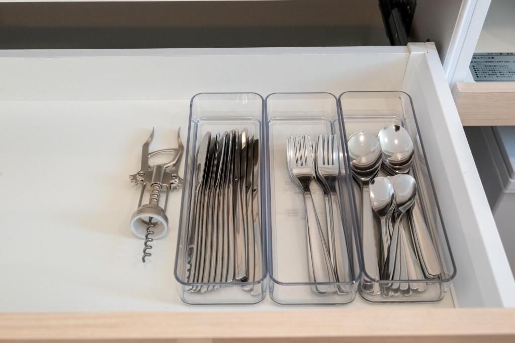 A drawer with clear plastic organizers containing utensils and a corkscrew.