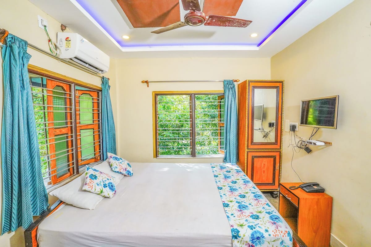 A bedroom with a bed, a wardrobe, a television, and an air conditioning unit.