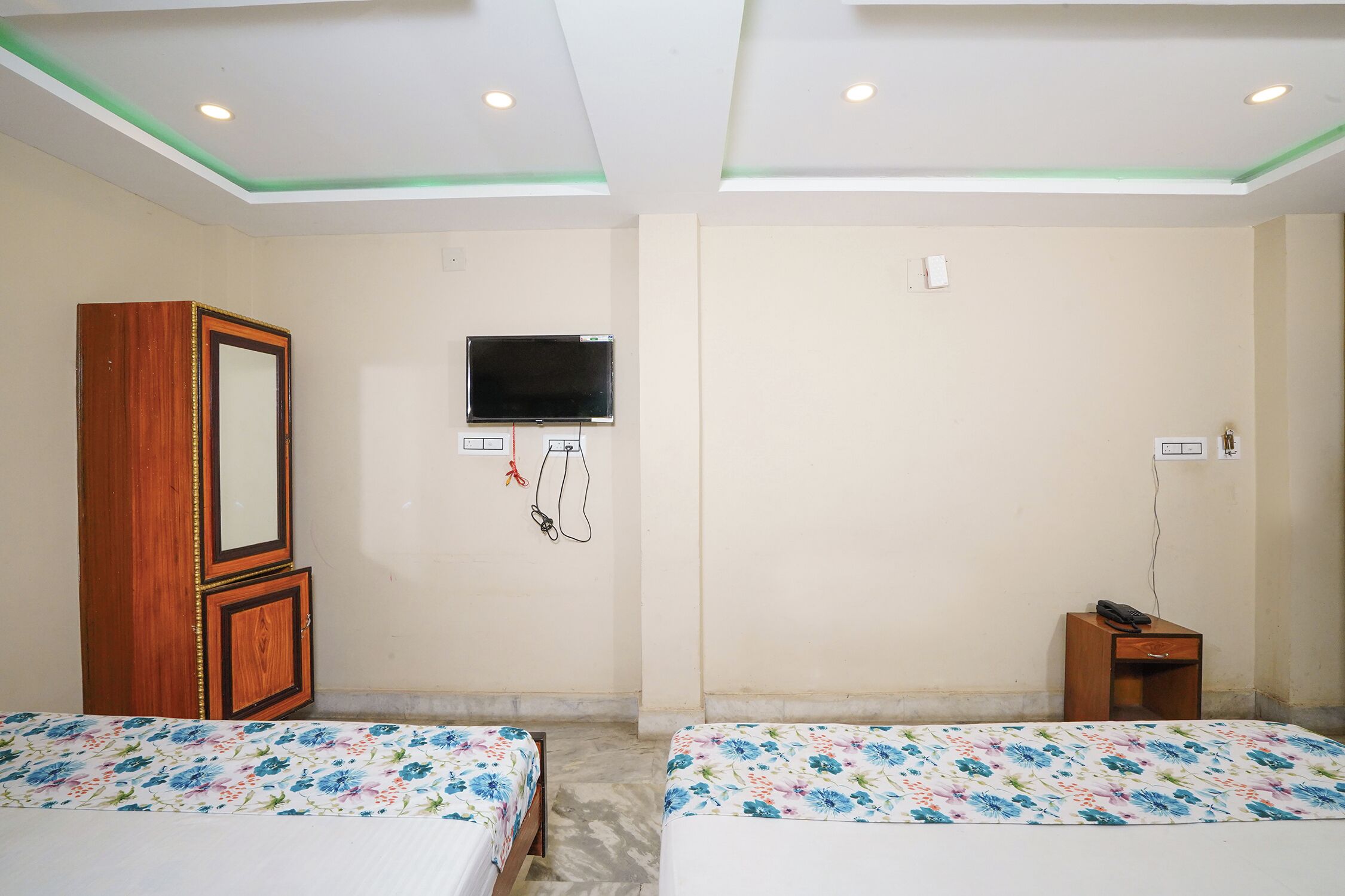 Una habitación con dos camas, un armario de madera, un televisor montado en la pared y una pequeña mesa de madera.