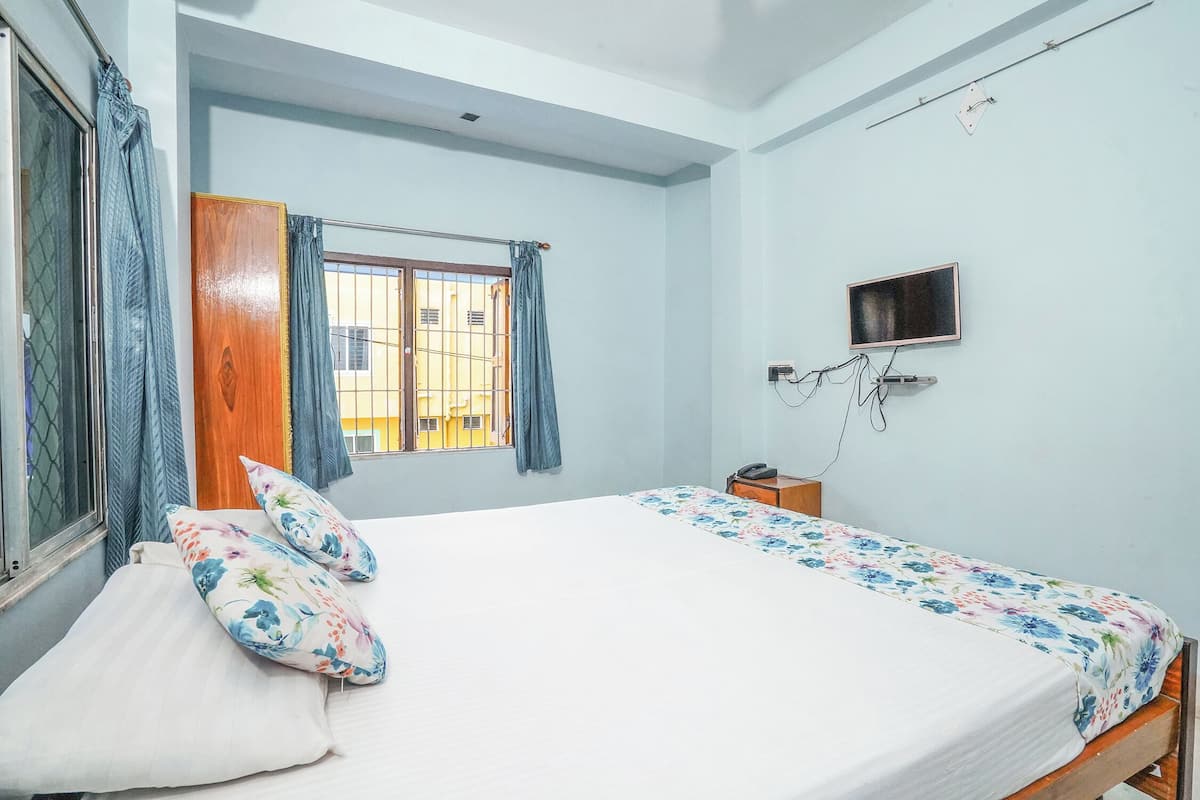A bedroom with a bed, a TV mounted on the wall, and a window with curtains.