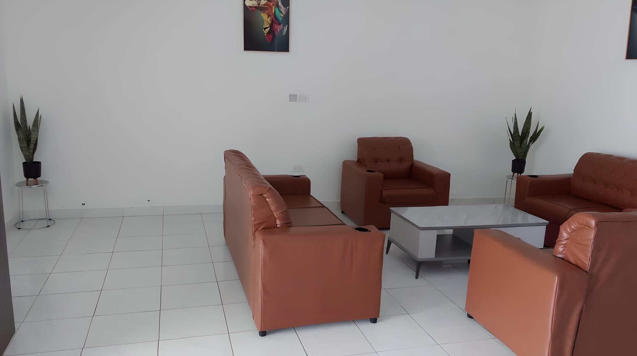 A modern living room with a sofa, armchairs, and a coffee table. There are potted plants and a painting on the wall.