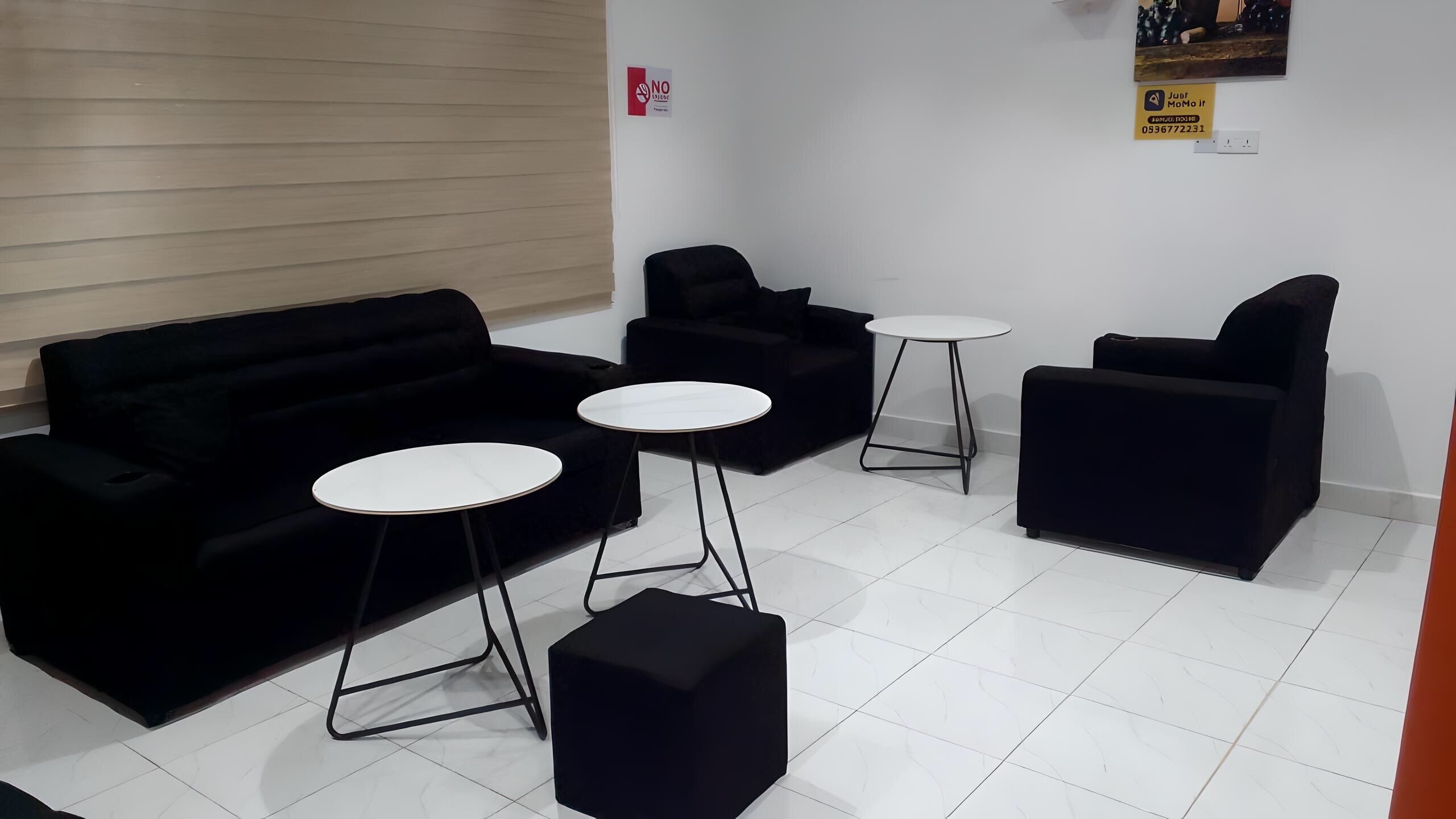 A room with a black sofa set, two round tables, and a black ottoman.