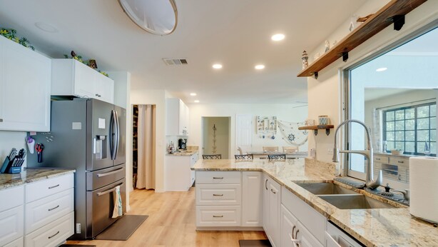 Una cocina moderna con gabinetes blancos, un refrigerador de acero inoxidable y una encimera de granito.