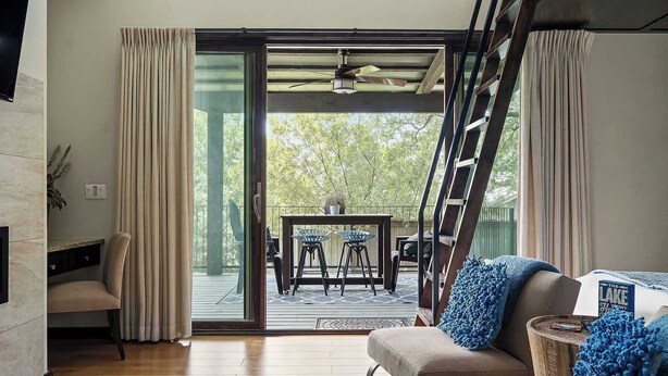 A modern living room with a sofa, a coffee table, and a TV. There is a sliding glass door leading to an outdoor patio with a table and chairs. - Charming Lake Getaway with Loft / Pickleball / BBQ (Lake Travis)