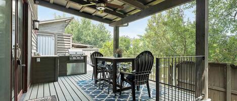A covered outdoor deck with a grill, chairs, and a table.