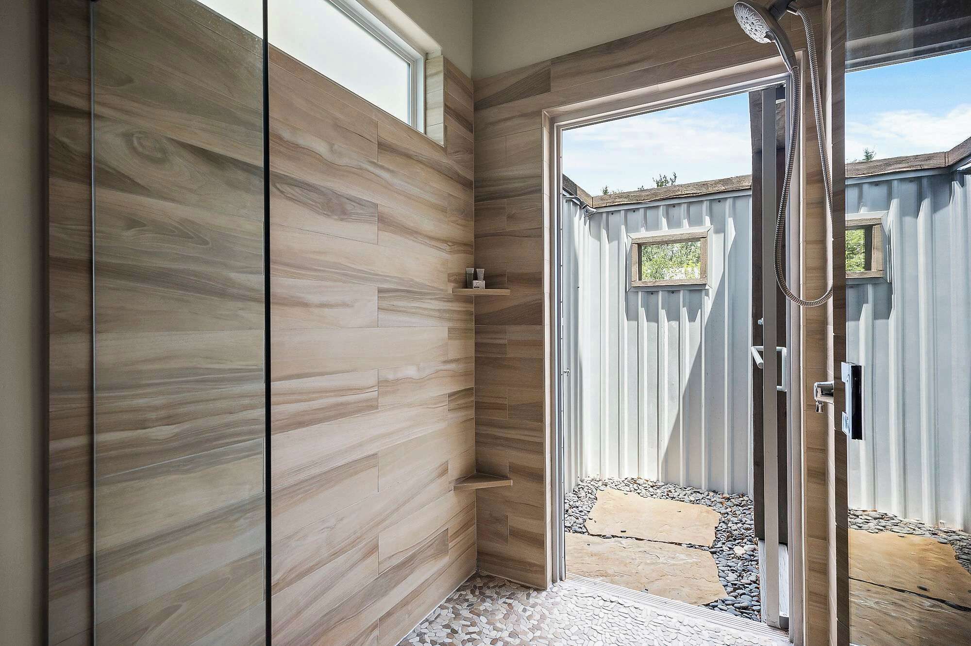 Un baño moderno con paneles de madera, zona de ducha y vista a un jardín trasero.