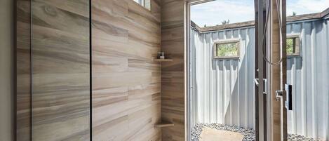 Un baño moderno con paneles de madera, zona de ducha y vista a un jardín trasero.