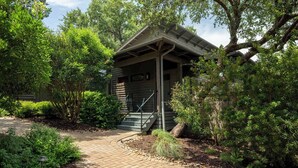 A rustic cabin with a porch, surrounded by dense greenery and a paved pathway. - Charming Lake Getaway with Loft / Pickleball / BBQ (Lake Travis)