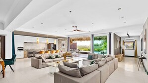 A spacious living area with a large sofa set, a dining table, and a kitchen in the background.