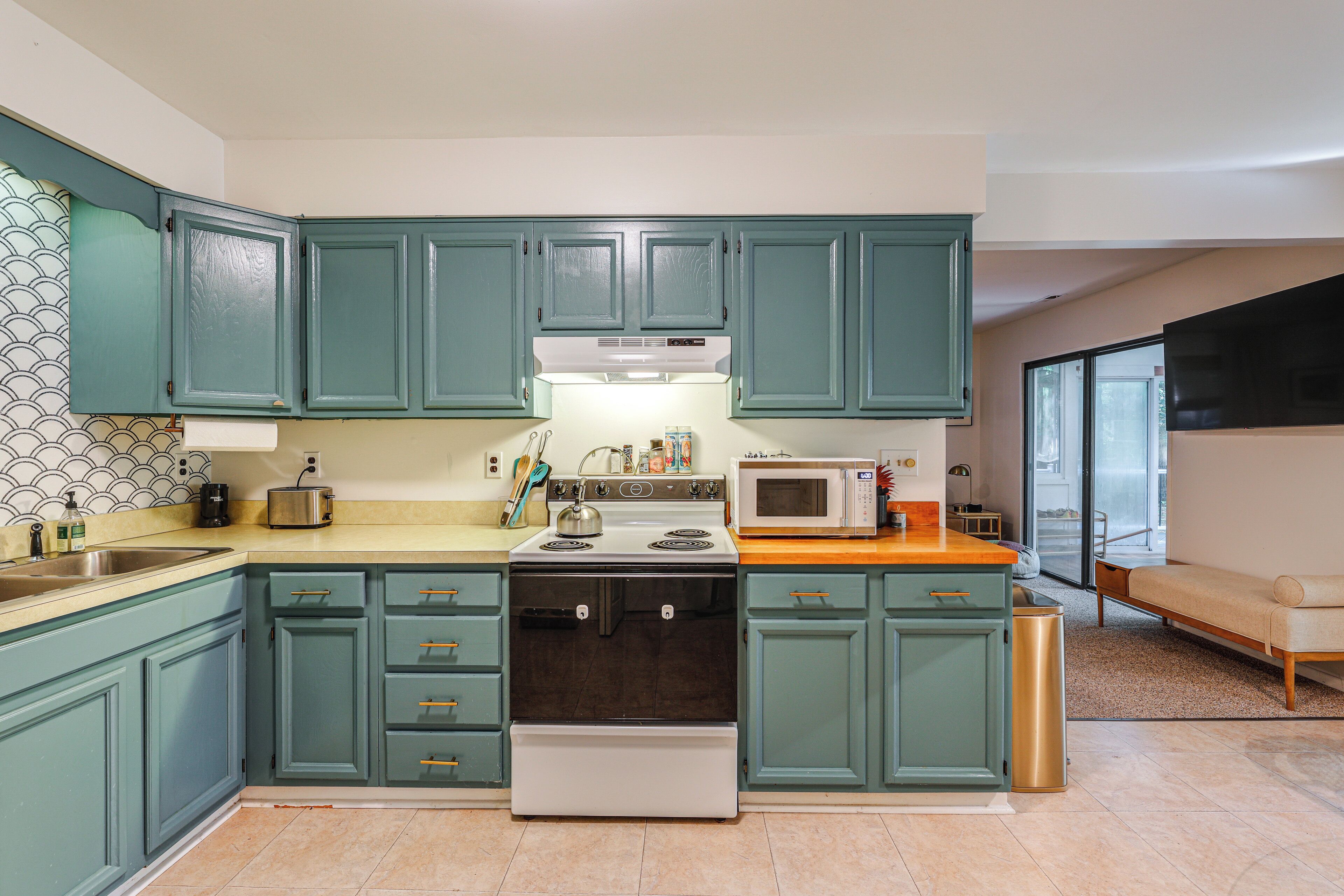 A kitchen with teal cabinets, a stove, a microwave, and a sink.
