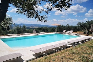 A swimming pool with lounge chairs and an umbrella, surrounded by trees and a view of distant hills. - Villa Ovidia: A three-story age-old farm house surrounded by the greenery, with Free WI-FI. (Assisi)